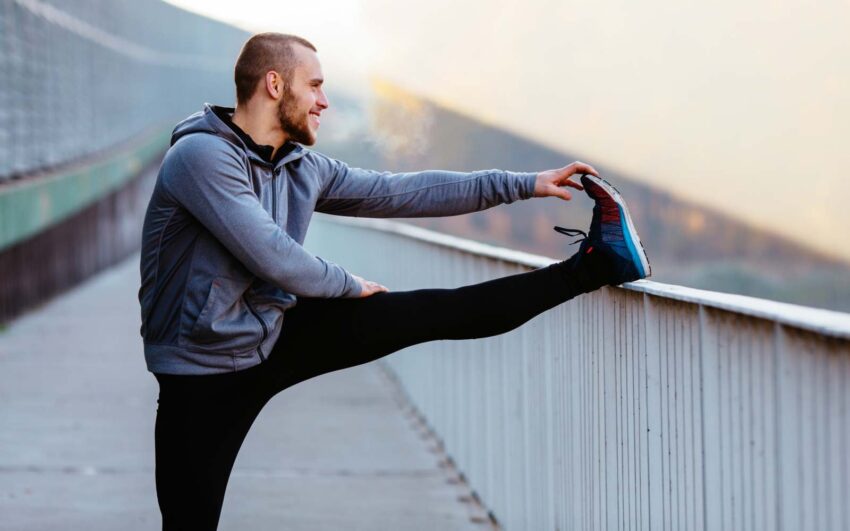 runner con leggins nero e felpa grigia fa stretching su una ringhiera bianca