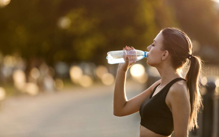 runner donna con top nero bere da una bottiglia acqua