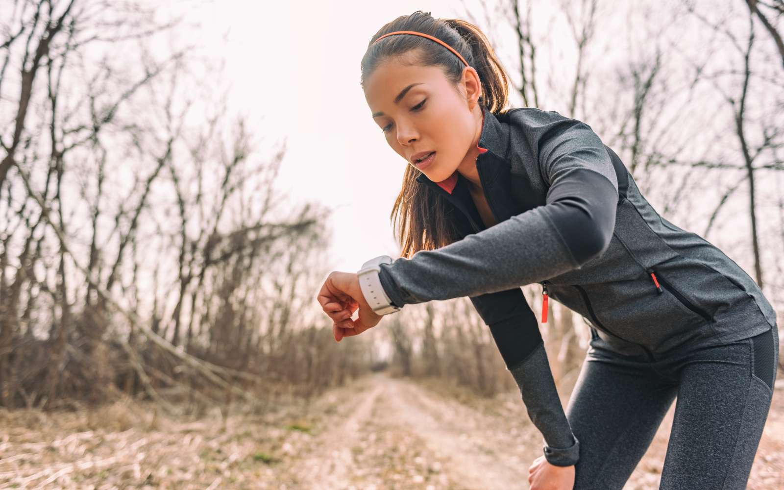 ragazza vestita con abbigliamento tecnico grigio da running guarda l'orologio tra un esercizio e l'altro