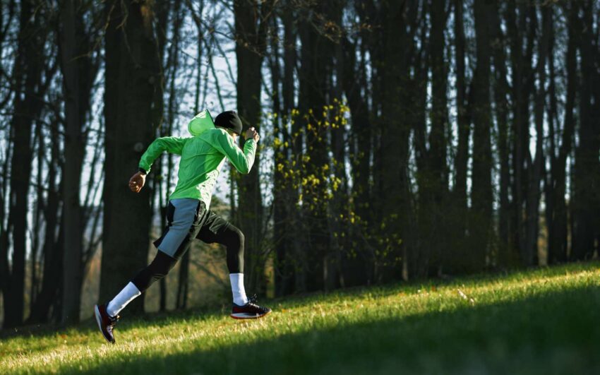 runner con abbiglaimento tecnico corre in salita nel bosco per migliora la resistenza