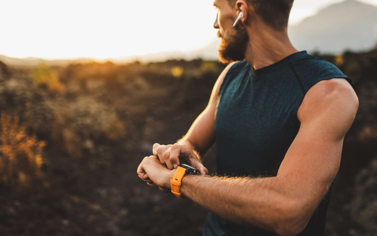 runner con canotta e cuffie senza filo controlla la frequenza cardiaca sull'orologio