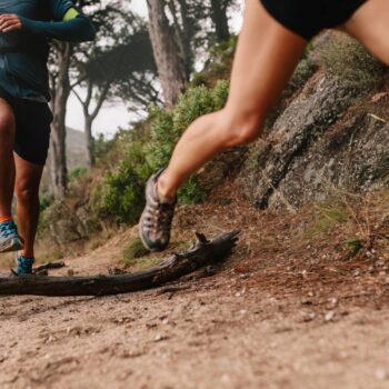 Healthy young couple running on mountain trail in morning. Young man and woman jogging on country path, focus on legs.