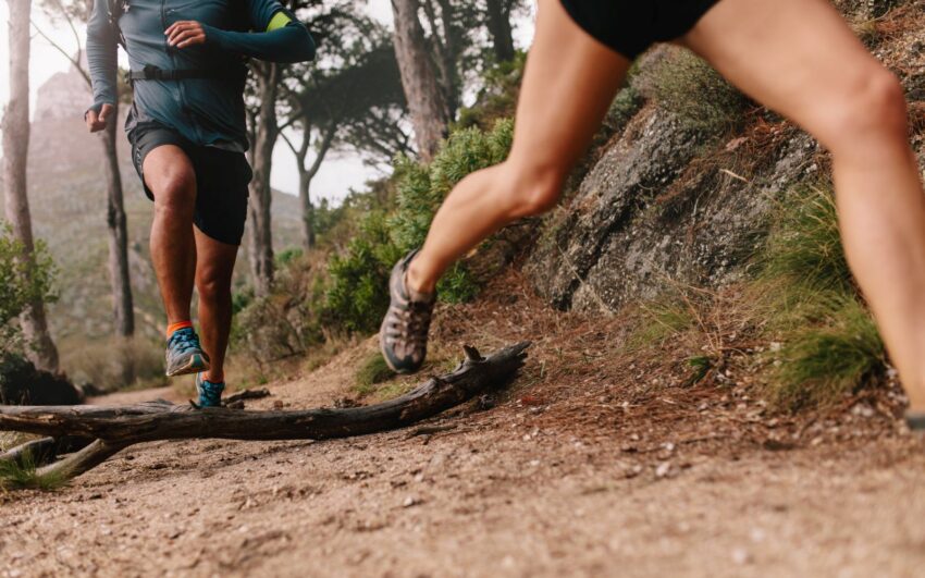 Healthy young couple running on mountain trail in morning. Young man and woman jogging on country path, focus on legs.